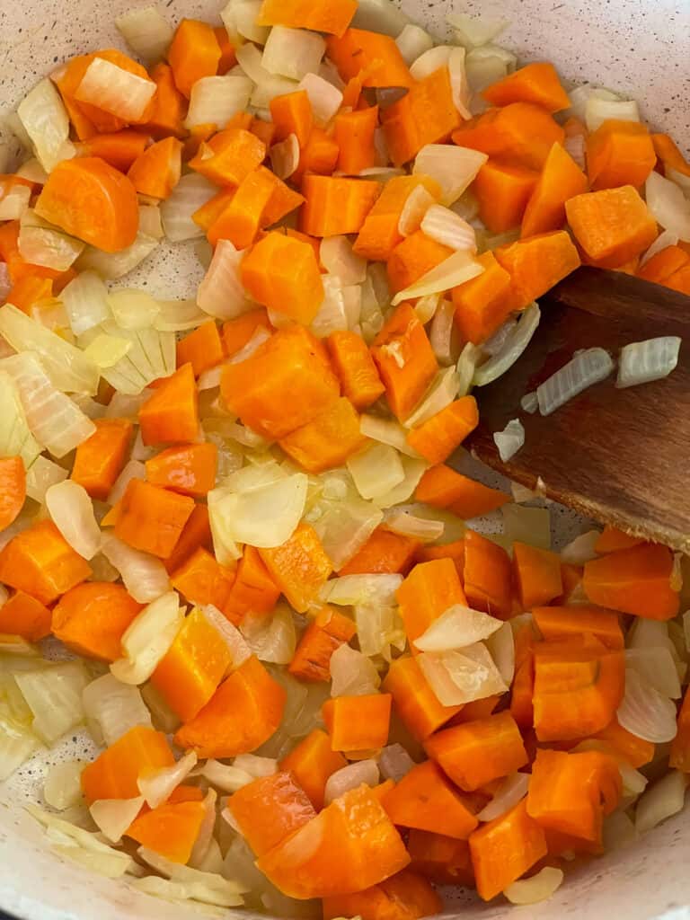 Carrots added to onions cooking in soup pot.