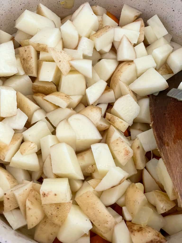 Cubed potatoes added to carrots and onions cooking in soup pot.