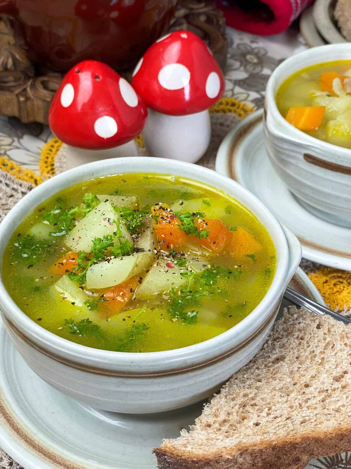 A bowl of soup with second bowl to side, bread to side, and toadstool salt shakers to side.