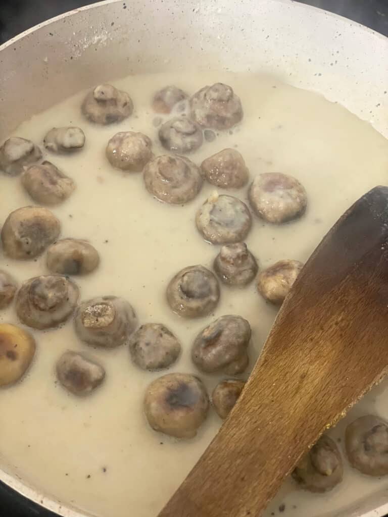 plant milk added to flour and mushrooms in pan.