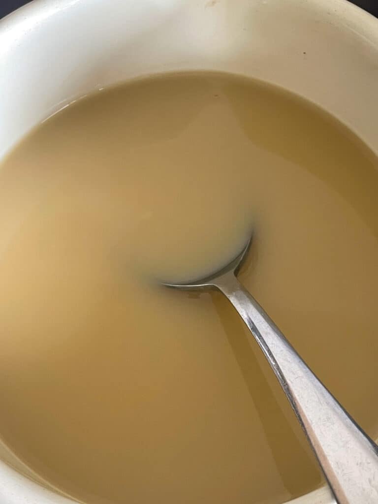 Syrup and plant milk stirred together in small bowl with spoon.