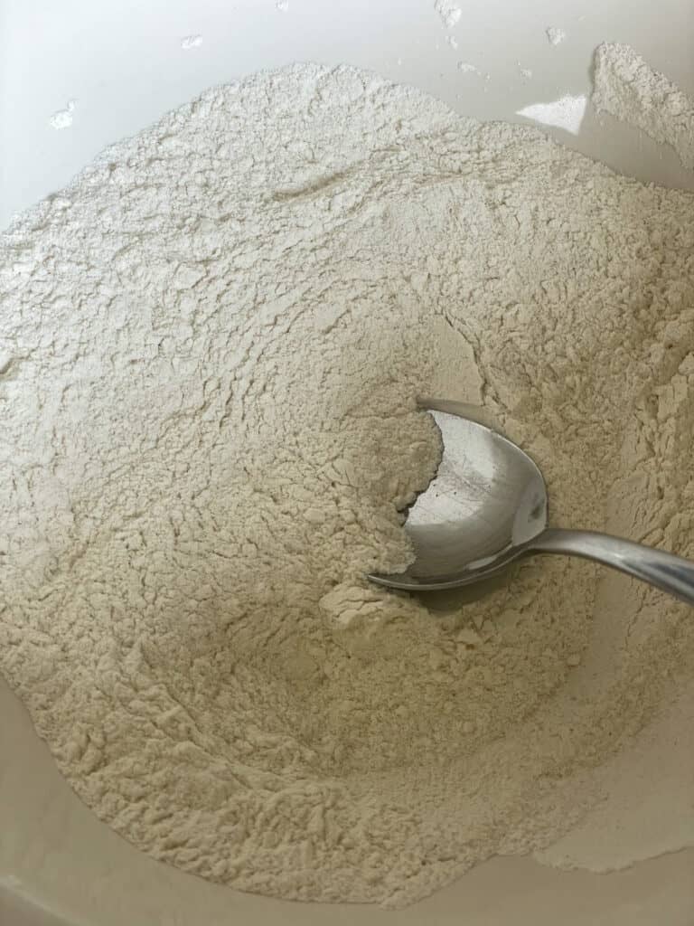 flour and bicarbonate of soda stirred together in mixing bowl with silver spoon.