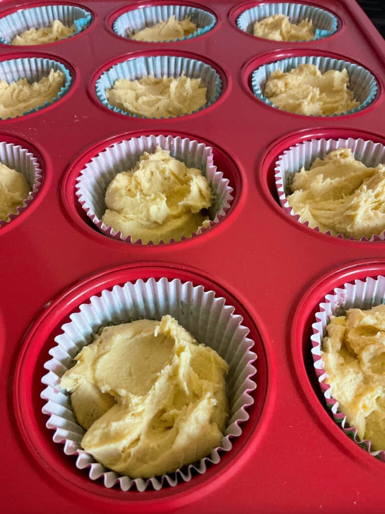 cake batter shared out between 12 cup muffin baking tray lined with paper cases.