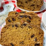 close up of slices of malt loaf on chopping board with flower, cottage and dog images, larger malt loaf to background, red and white check table cloth.