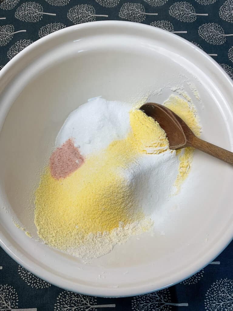 dry ingredients for cornbread in mixing bowl with wooden spoon to side.