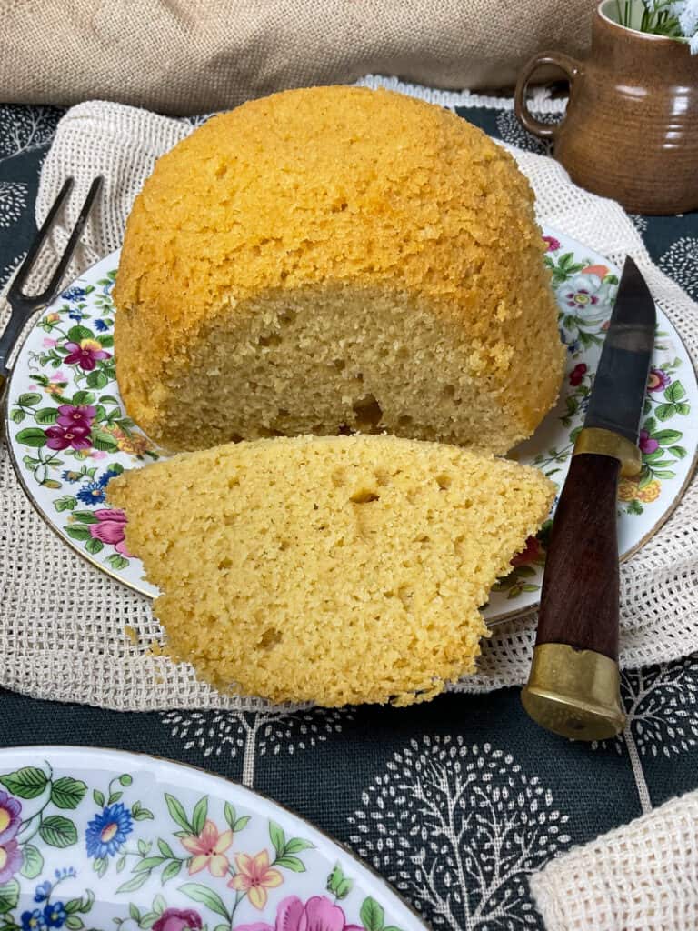 cornbread with a piece sliced off and on the plate, second plate to side with flower pattern.