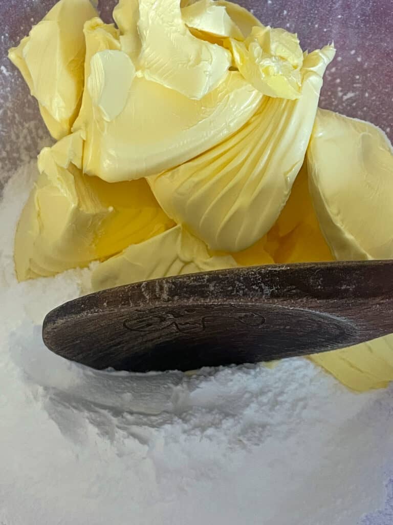 margarine and powdered sugar added to mixing bowl with wooden spoon.