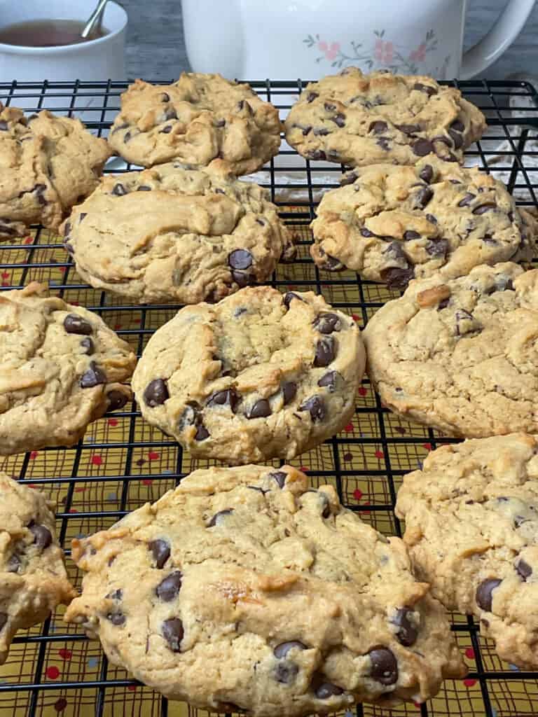 Chocolate chip cookies cooling on wire rack, with tea cup filled with tea and tea pot in background.