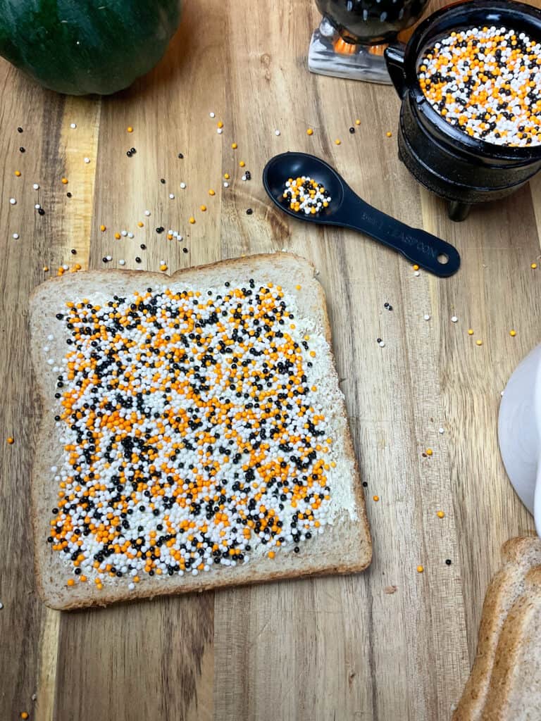 cake sprinkles added to buttered bread, small black teaspoon to side with sprinkles scattering out.