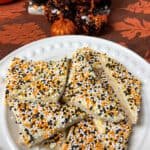 A white plate with sliced triangles of Halloween sprinkles Fairy bread, orange leave table runner and glittery pumpkin ornaments.