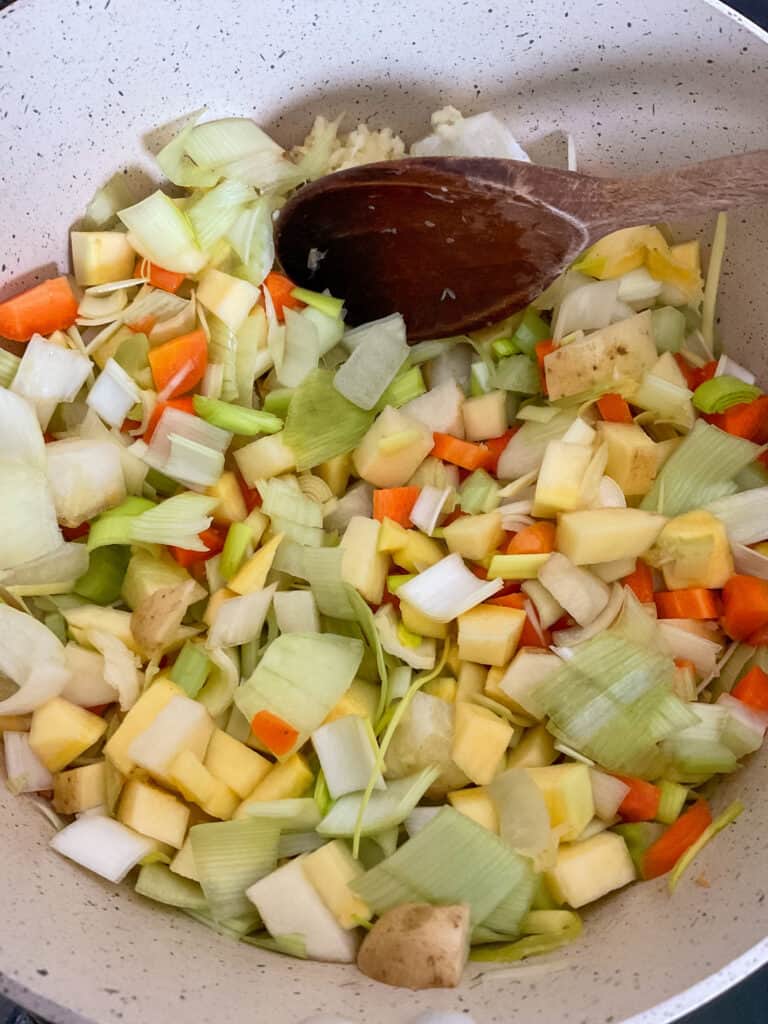 Diced vegetables in soup pan with wooden spoon.