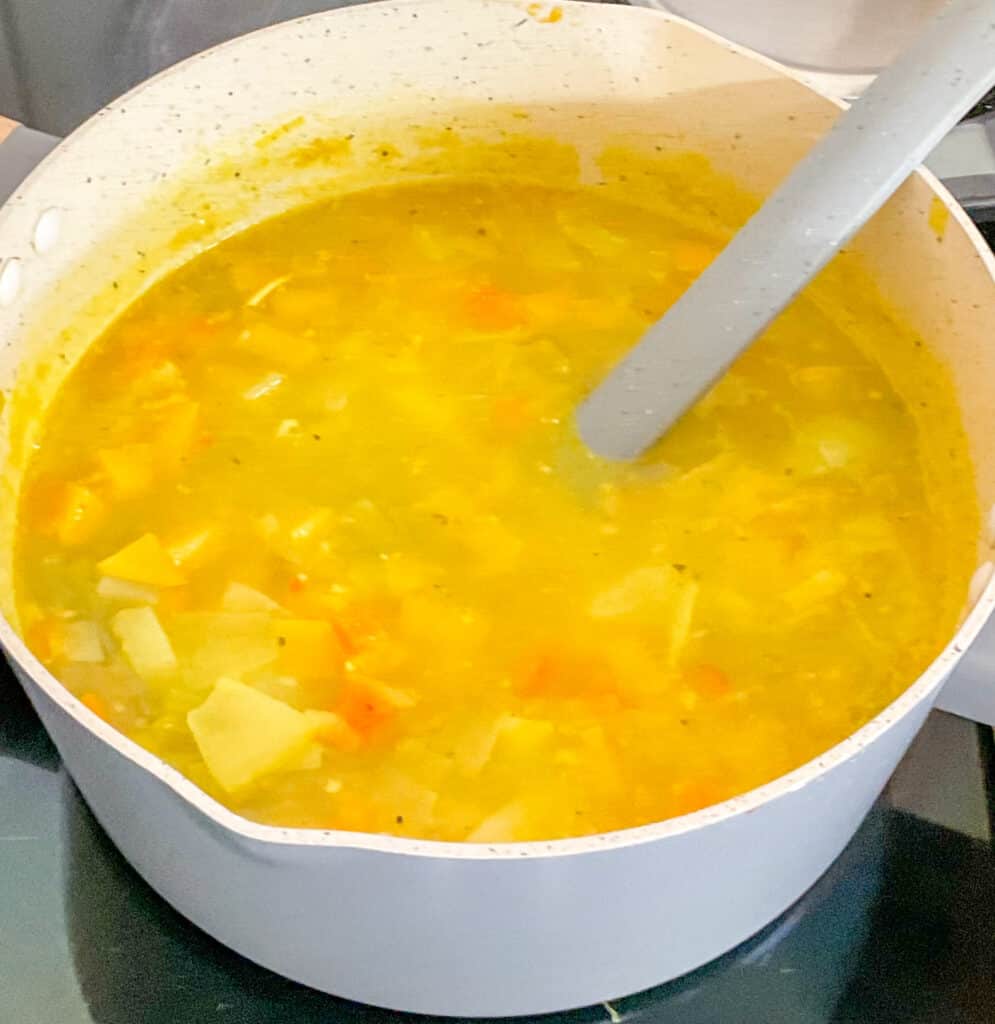 Soup simmered and cooked in saucepan with grey ladle on cooker top.