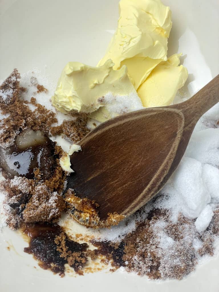 Sugar, margarine and vanilla in mixing bowl with wooden spoon.