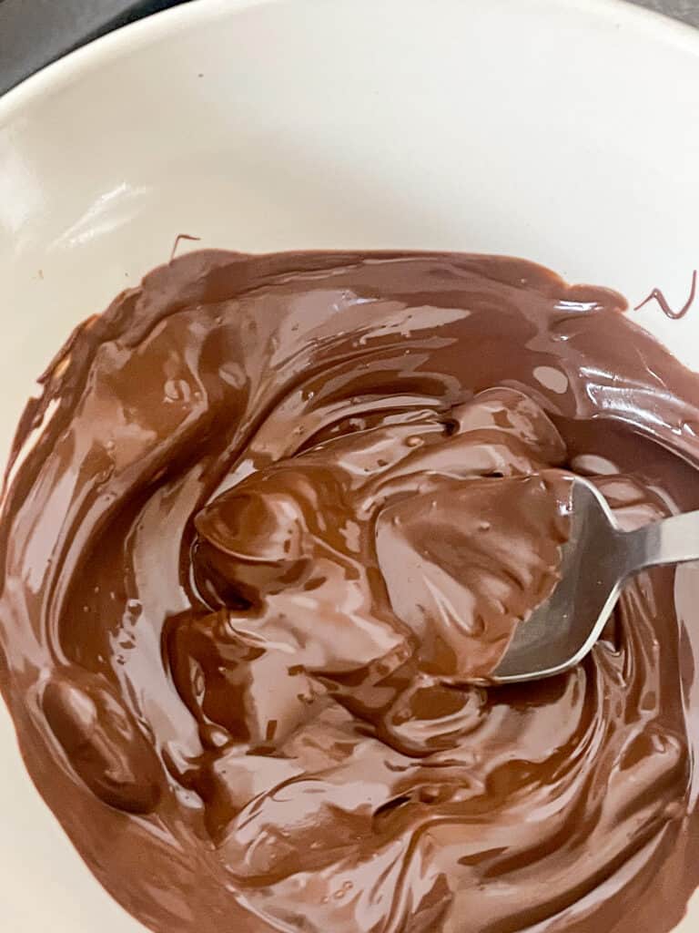 chocolate melted in pudding bowl and being mixed with small spoon.