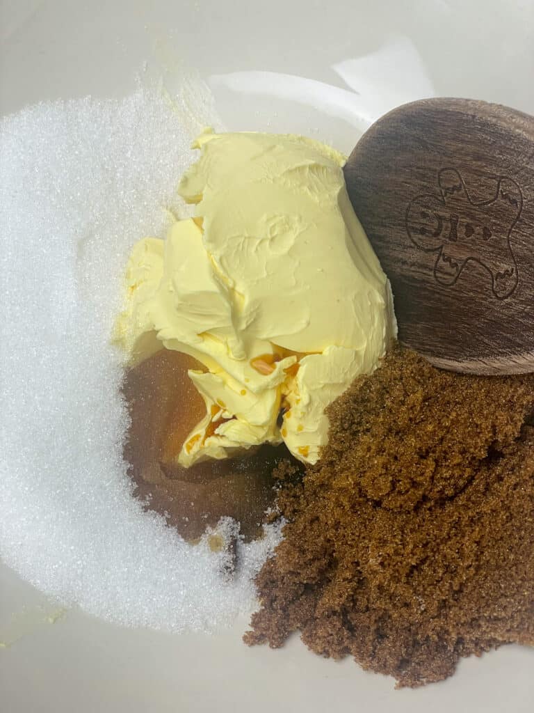 Sugar, margarine and vanilla in mixing bowl with wooden spoon.