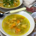 Close up bowl of vegetable soup with yellow handled spoon and second bowl in background, slices of bread to side on a mat with fox image.