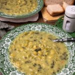 green flowered pattern bowl of old-fashioned pea soup with second bowl in background, loaf of fresh baked bread to side.
