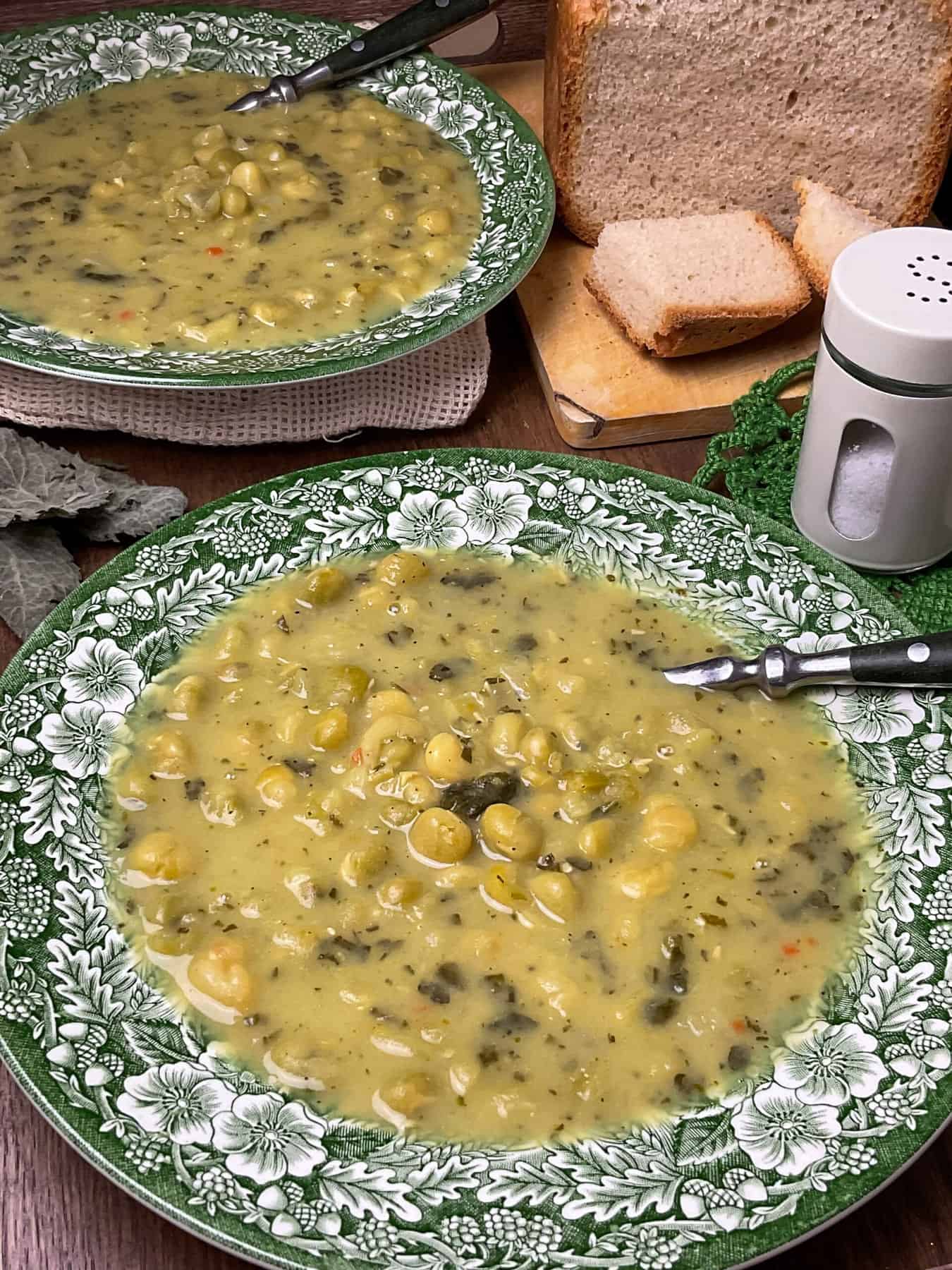 green flowered pattern bowl of old-fashioned pea soup with second bowl in background, loaf of fresh baked bread to side.