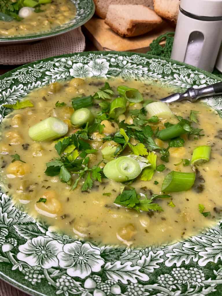 close up of pea soup garnished with parsley and spring onions, second bowl in background. 