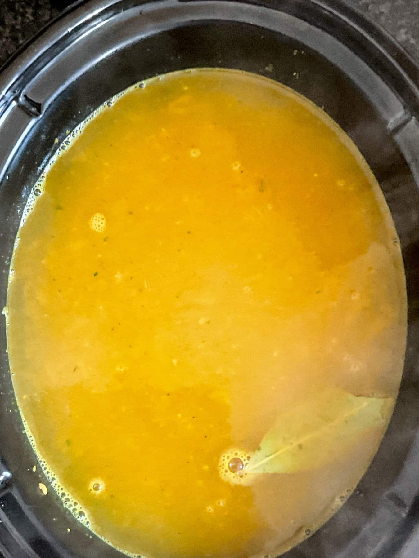 Vegetable stock poured into the slow cooker with red lentil dal ingredients.