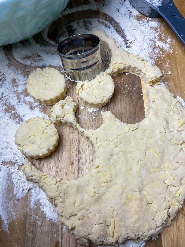 cobbler dough rolled out and biscuit cutter stamping out circles on floured wooden board.