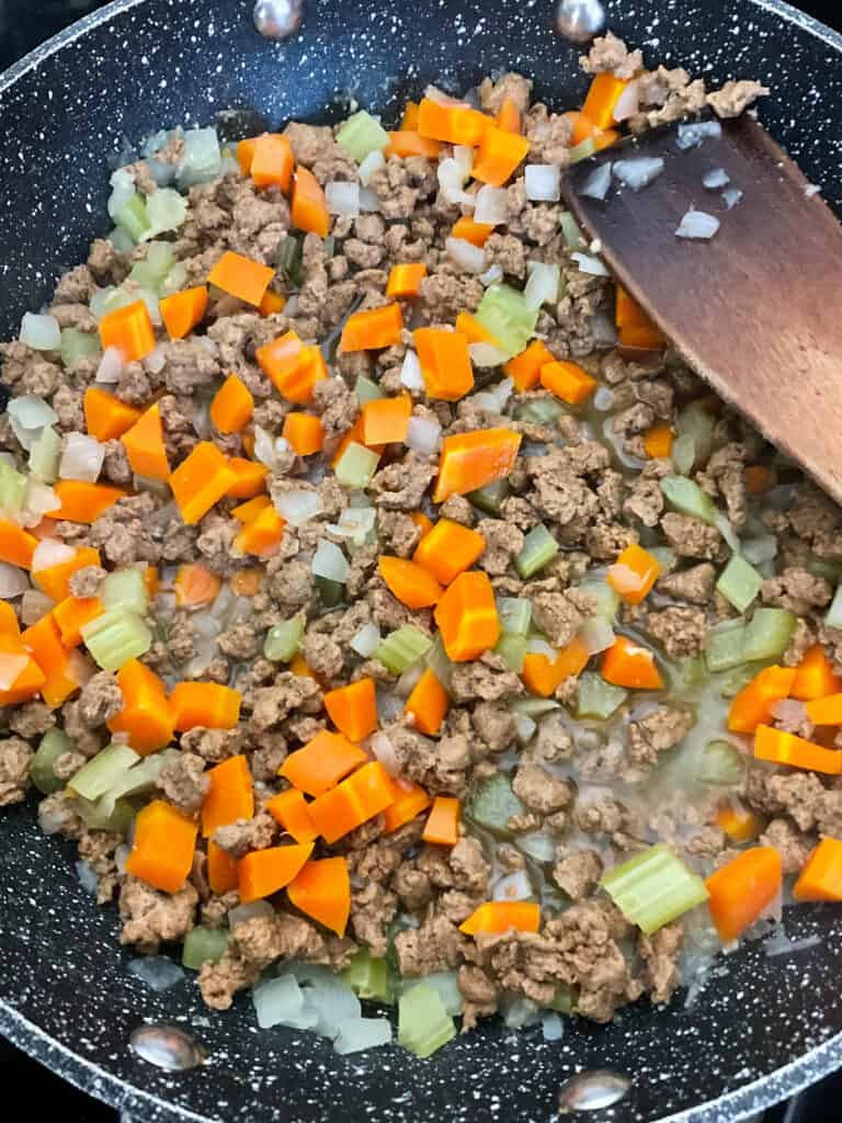Vegan mince added to veggies in skillet with wooden spatula.
