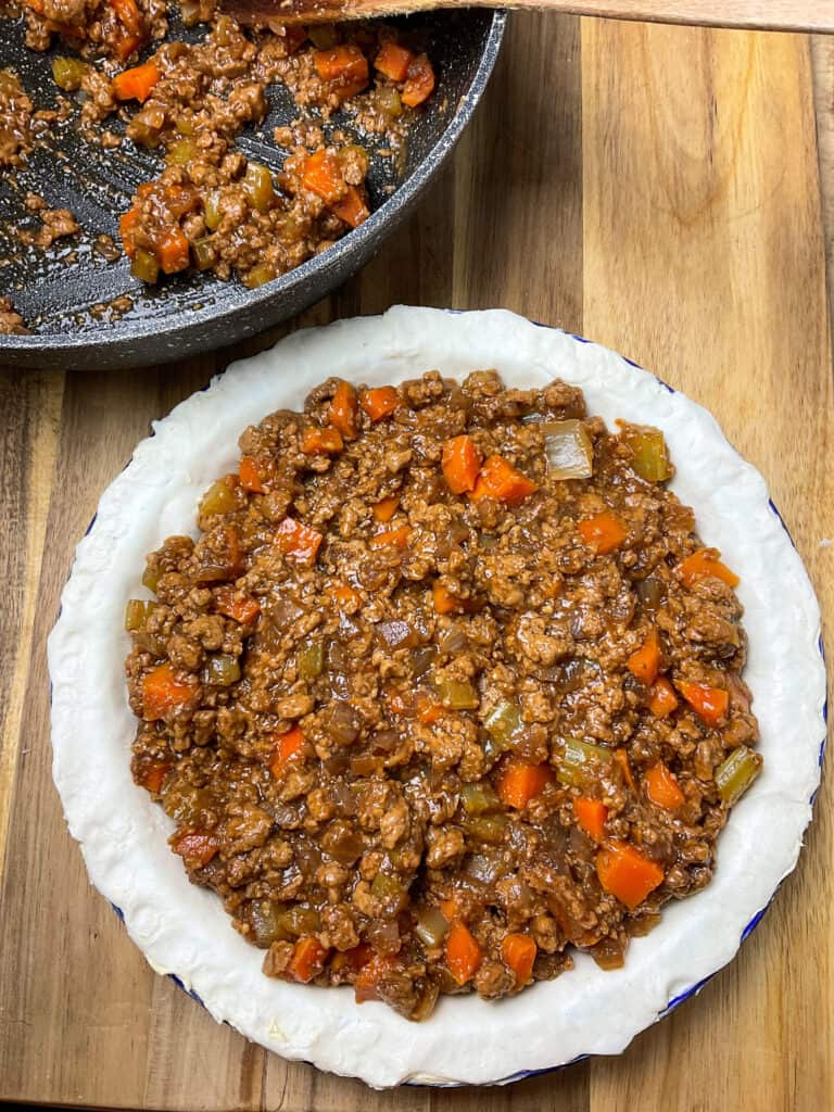 Filling added to lined pie dish with skillet to side.