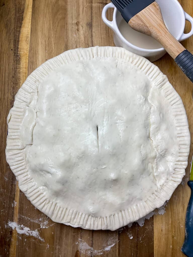Lid of pastry over top of pie dish, with small bowl of milk and pastry brush to side.