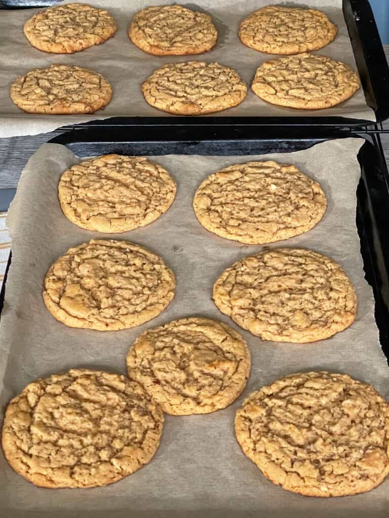 two trays of peanut butter cookies on parchment paper just out of the oven.