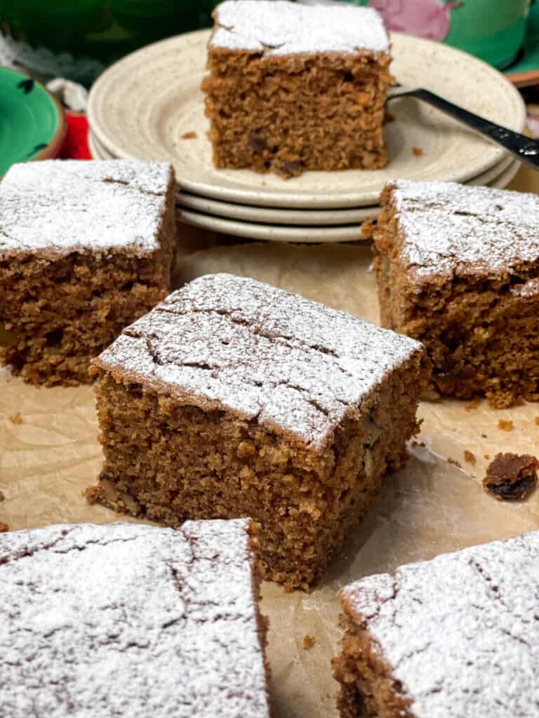 slices of applesauce cake on a wooden board with one slice on top of three cream coloured cake plates and cake fork.