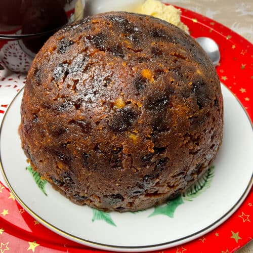 Close up of vegan slow cooker Christmas pudding on a festive plate and a red circular serving tray.