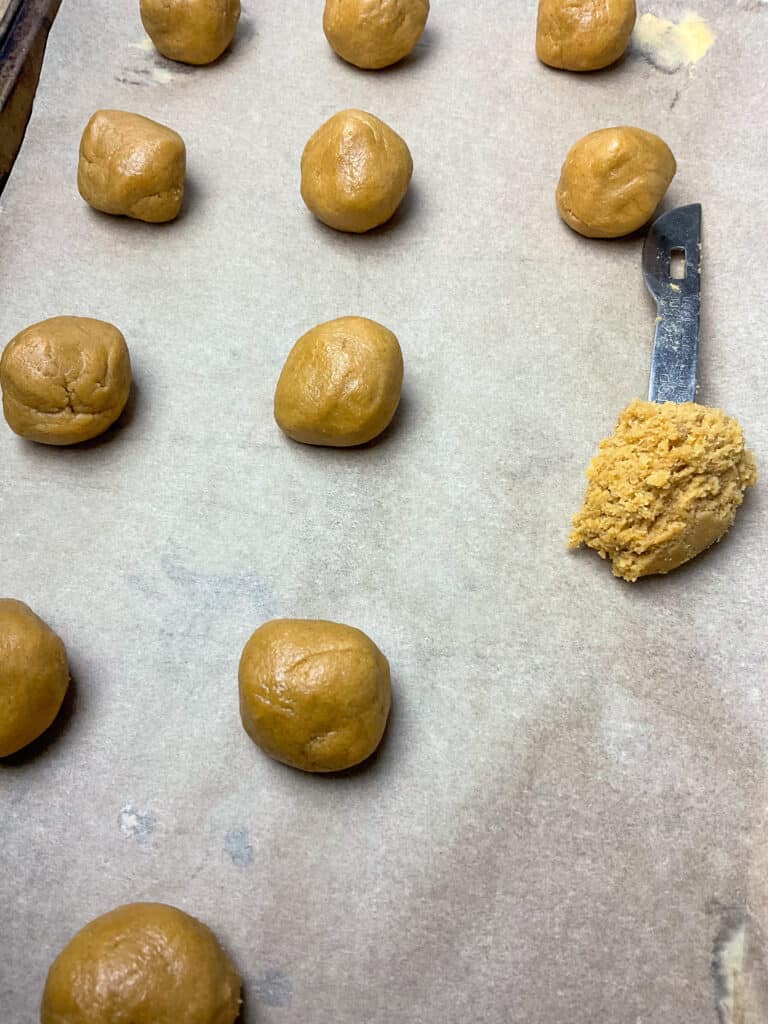balls of gingerbread cookie dough on baking tray with teaspoon scooped full of dough.