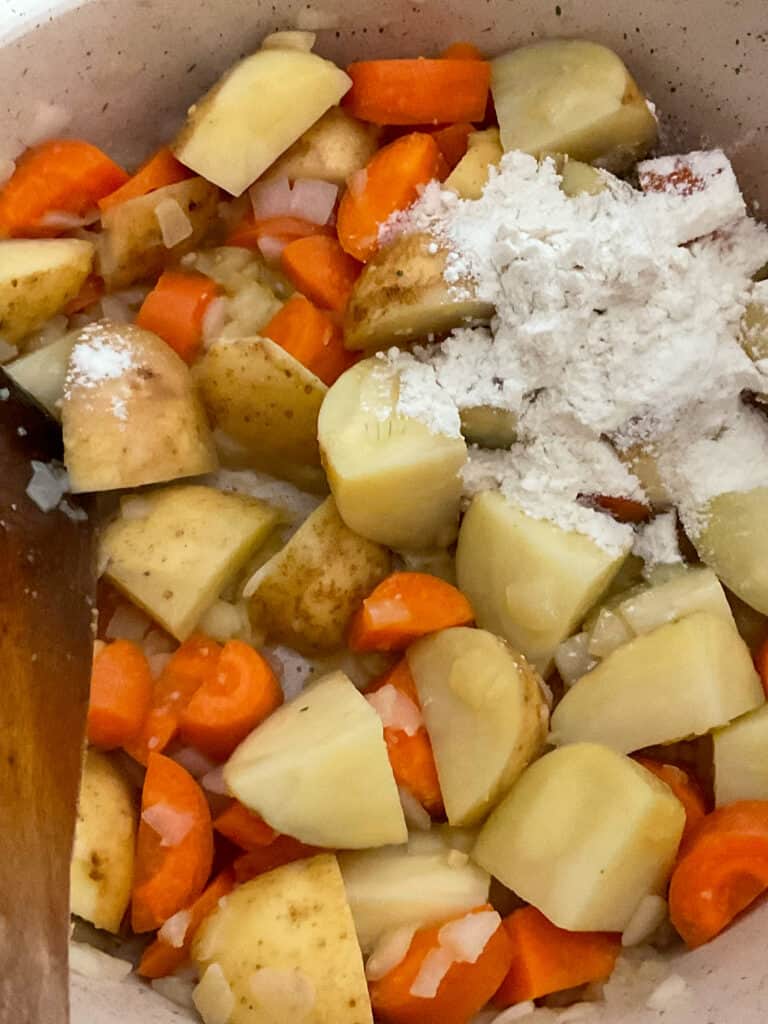 flour added to veggies cooking in pot with wooden spatula.