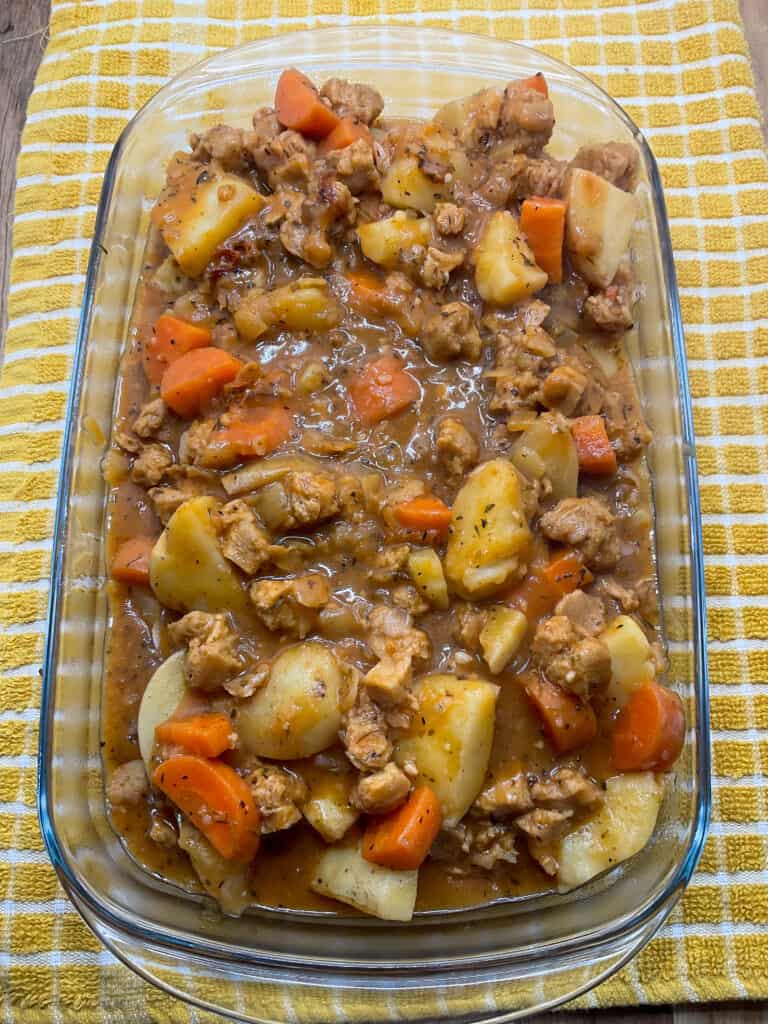 meat and potato pie stew filling added to rectangular Pyrex dish, yellow and white check patterned tea cloth background.