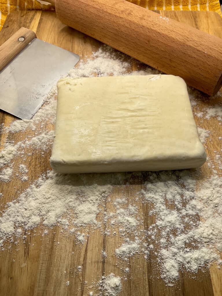 puff pastry block on floured wooden board with rolling pin.