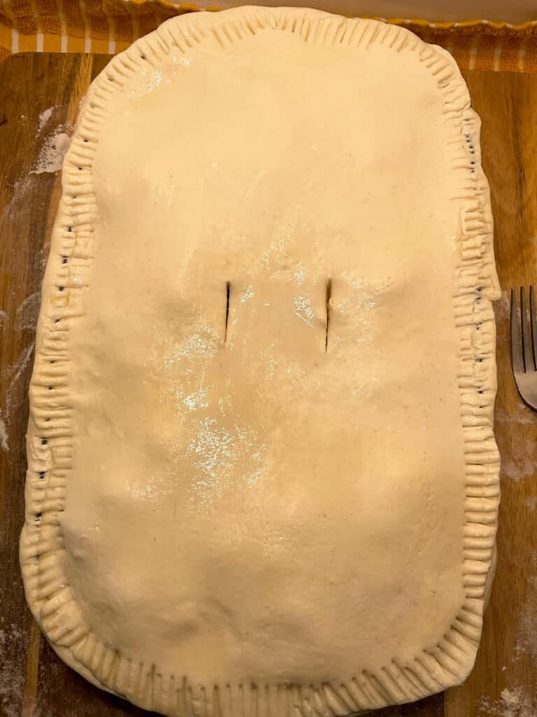 puff pastry lid covering the pie dish, and the edges crimped and two slits added to pie to allow steam to escape.