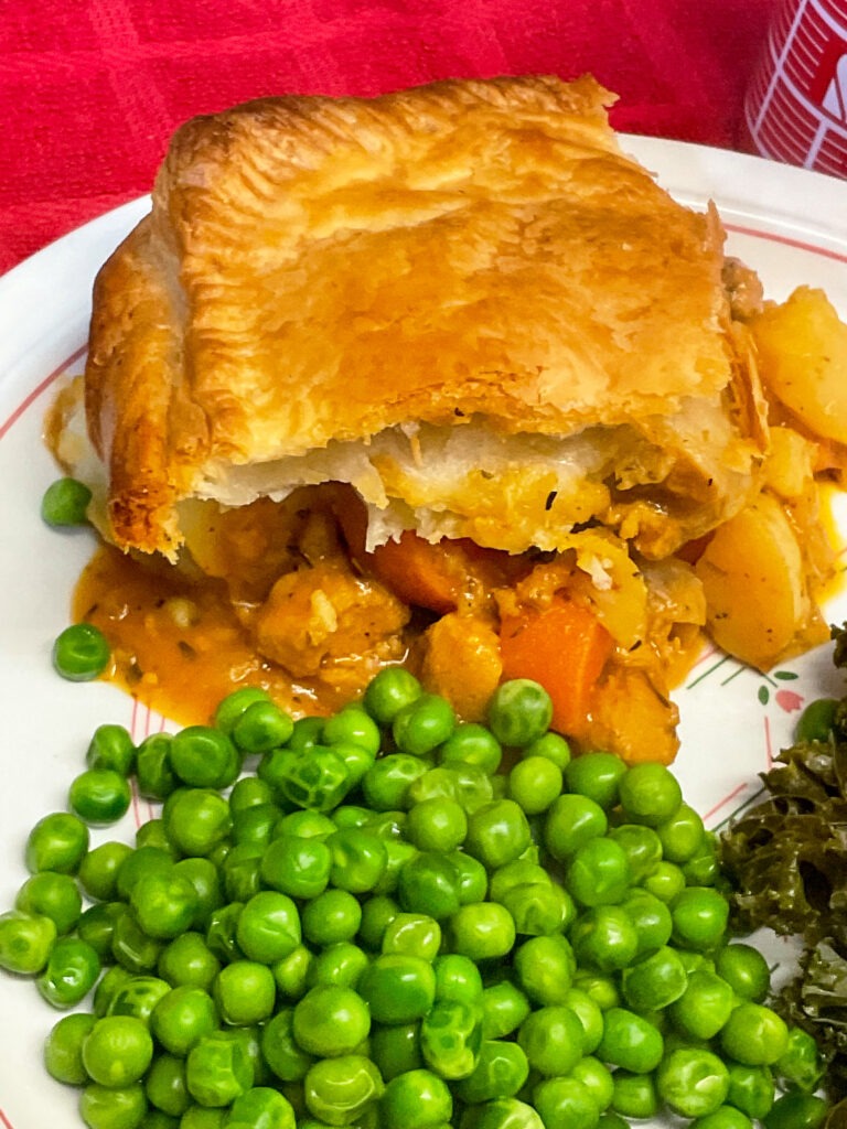 vegan meat and potato pie served with peas and kale, red table mat background.