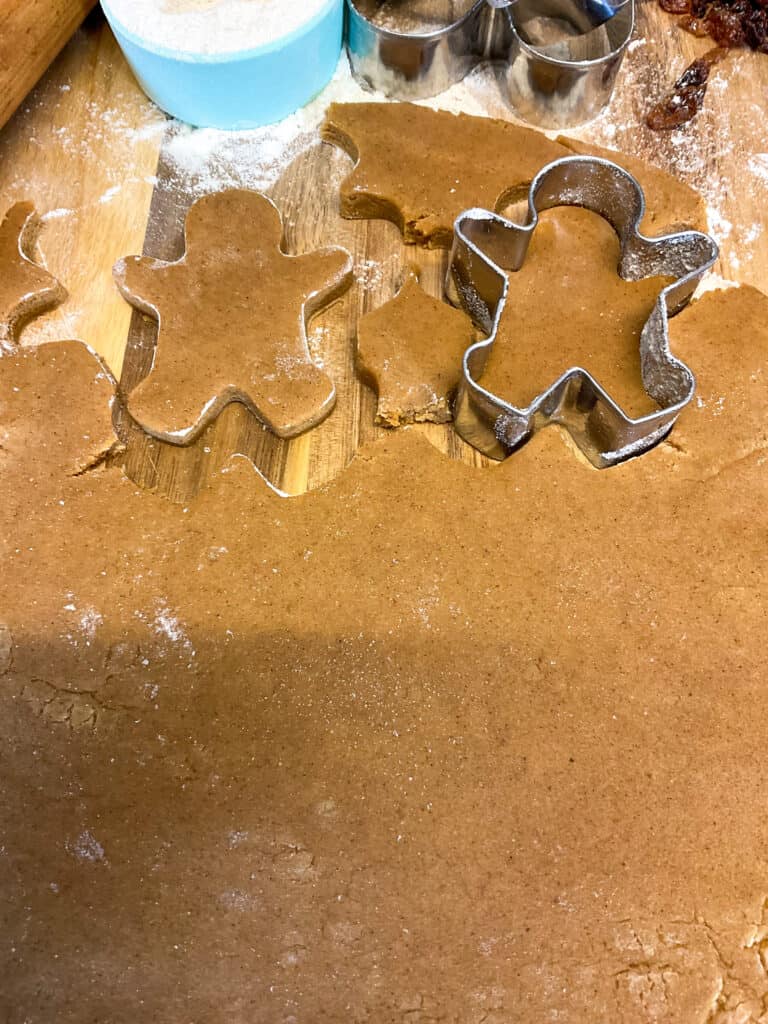 gingerbread men cookie dough rolled out and two gingerbread men cookies stamped out.