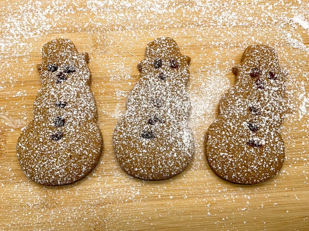 three gingerbread snowmen dusted with powdered sugar to emulate a snow blizzard, on wooden board.