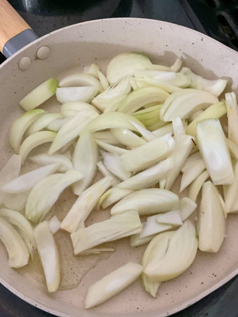 Sliced onions cooking in cream coloured fry pan on stove top.