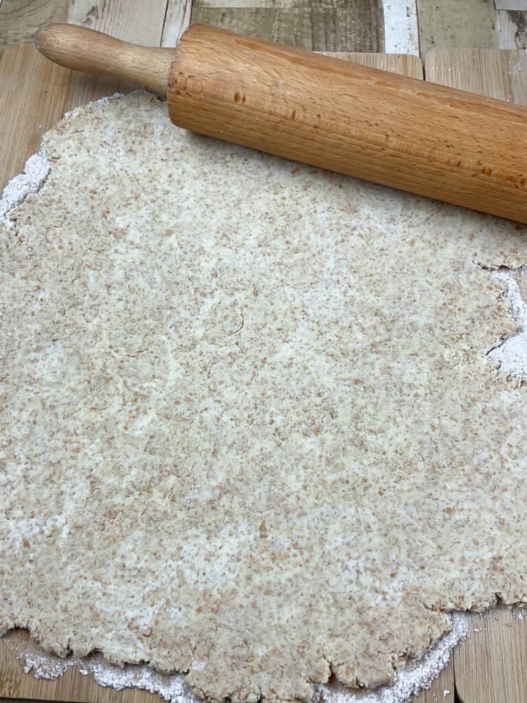 pastry dough rolled out on floured board with wooden rolling pin.