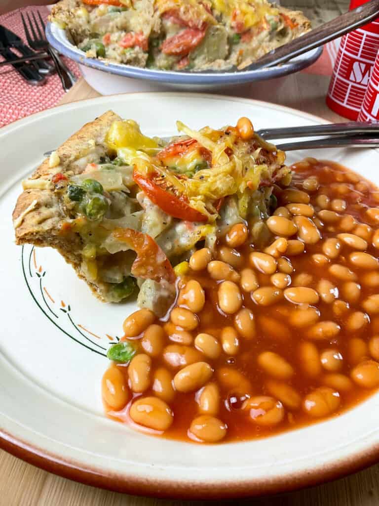 Dinner plate with a slice of homity pie and baked beans, with pie dish in background.