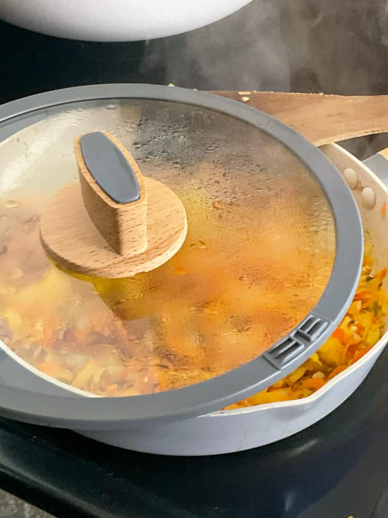lid placed over skillet pan with veggies sauteing on the cooker stove-top. 