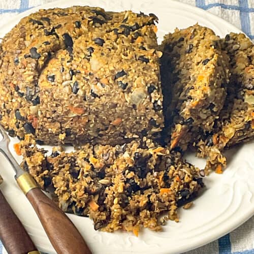 Vegan haggis on a white serving plate with slices cut, brown handled knife to side and blue and white check table cloth background.