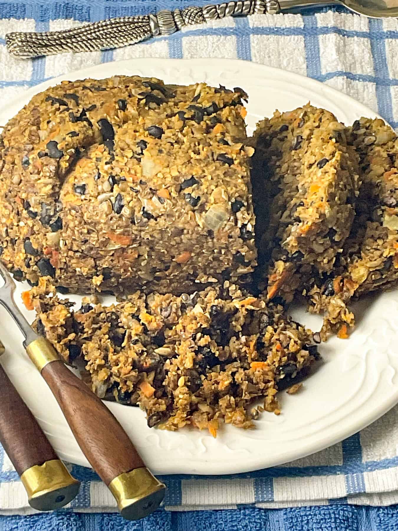 Vegan haggis on a white serving plate with slices cut, brown handled knife to side and blue and white check table cloth background.