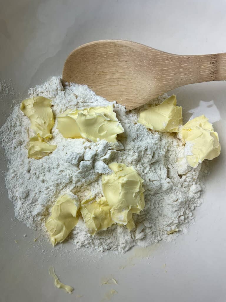 Margarine in mixing bowl with flour, wooden spoon to side.