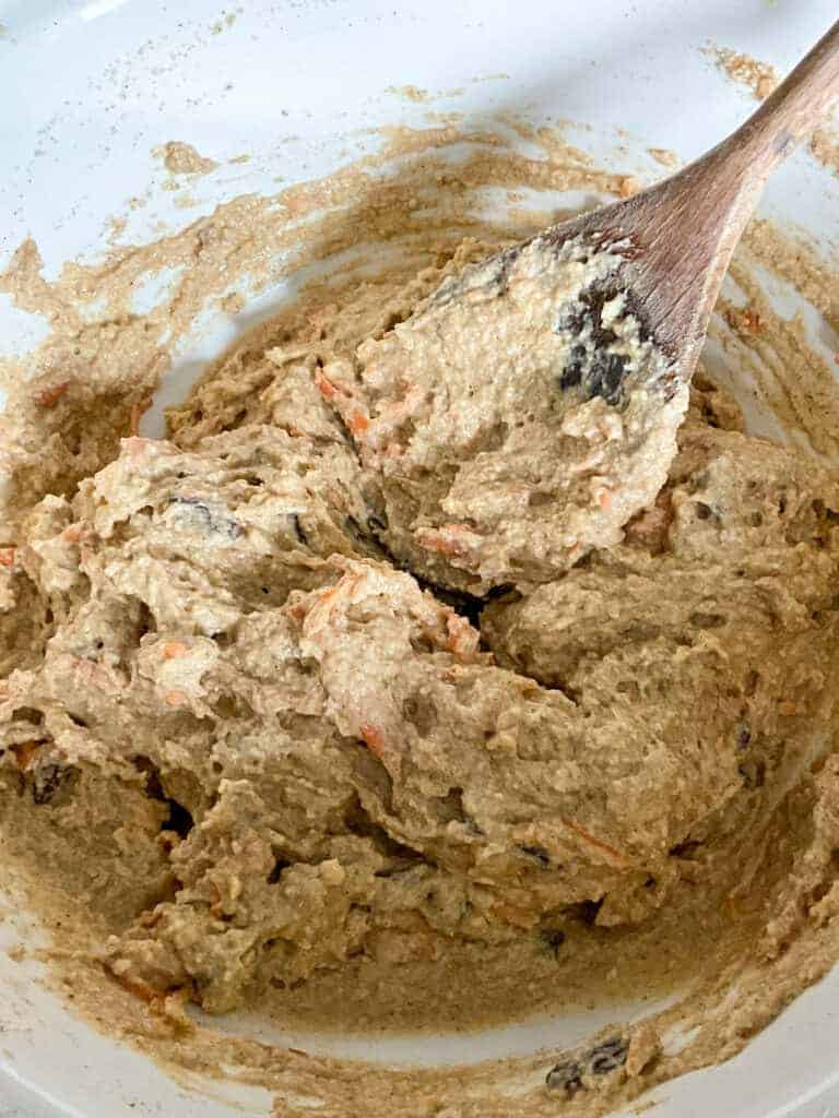 Wet ingredients mixed through dry ingredients in bowl with wooden spoon.