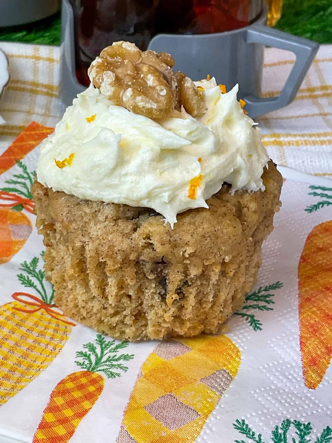 carrot cupcake featured image, one carrot cake sitting on a carrot image napkin with a picnic mug behind.
