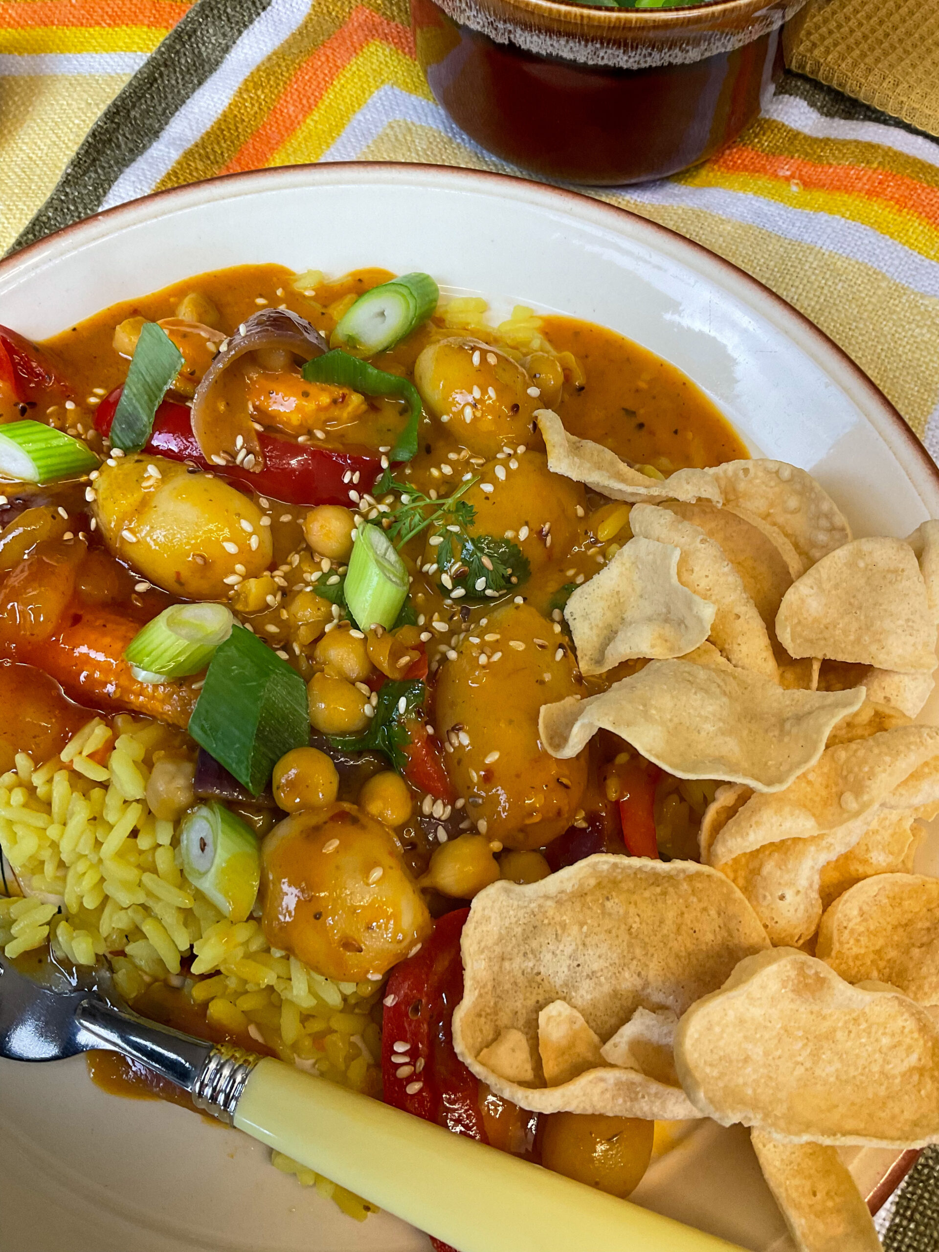 A dinner plate with a serving of mango curry, rice and crispy mini poppadum's.