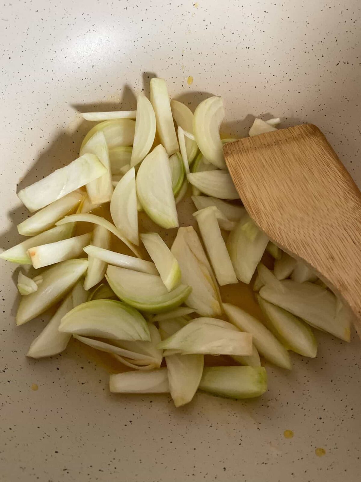 Onions sauteing in pan with wooden spatula.